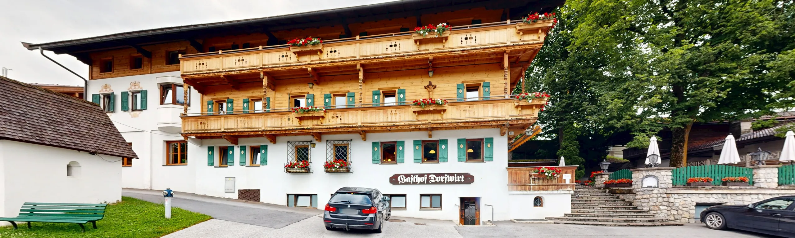 Traditionelles Gebäude mit Holzbalkonen, umgeben von Bäumen und einer blühenden Umgebung.
